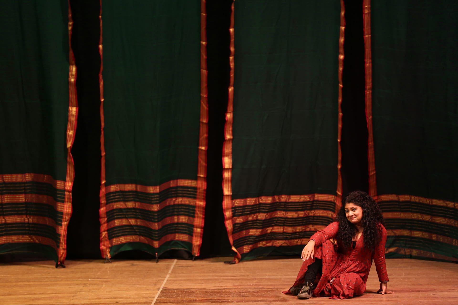 Manasi Joshi as Dr. Anandibai — seated on stage with traditional textile backdrop