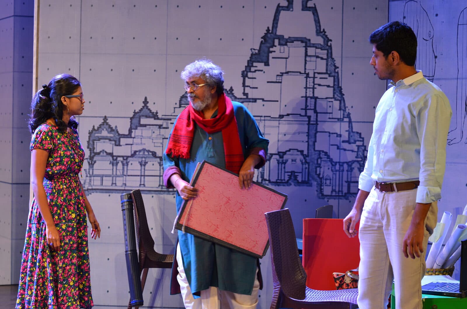 Bhanushankar Sompura holds a drawing board in the architect's office, flanked by his son and Tanvi